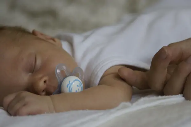newborn baby sleeping in a white onsies with yellowing of the skin