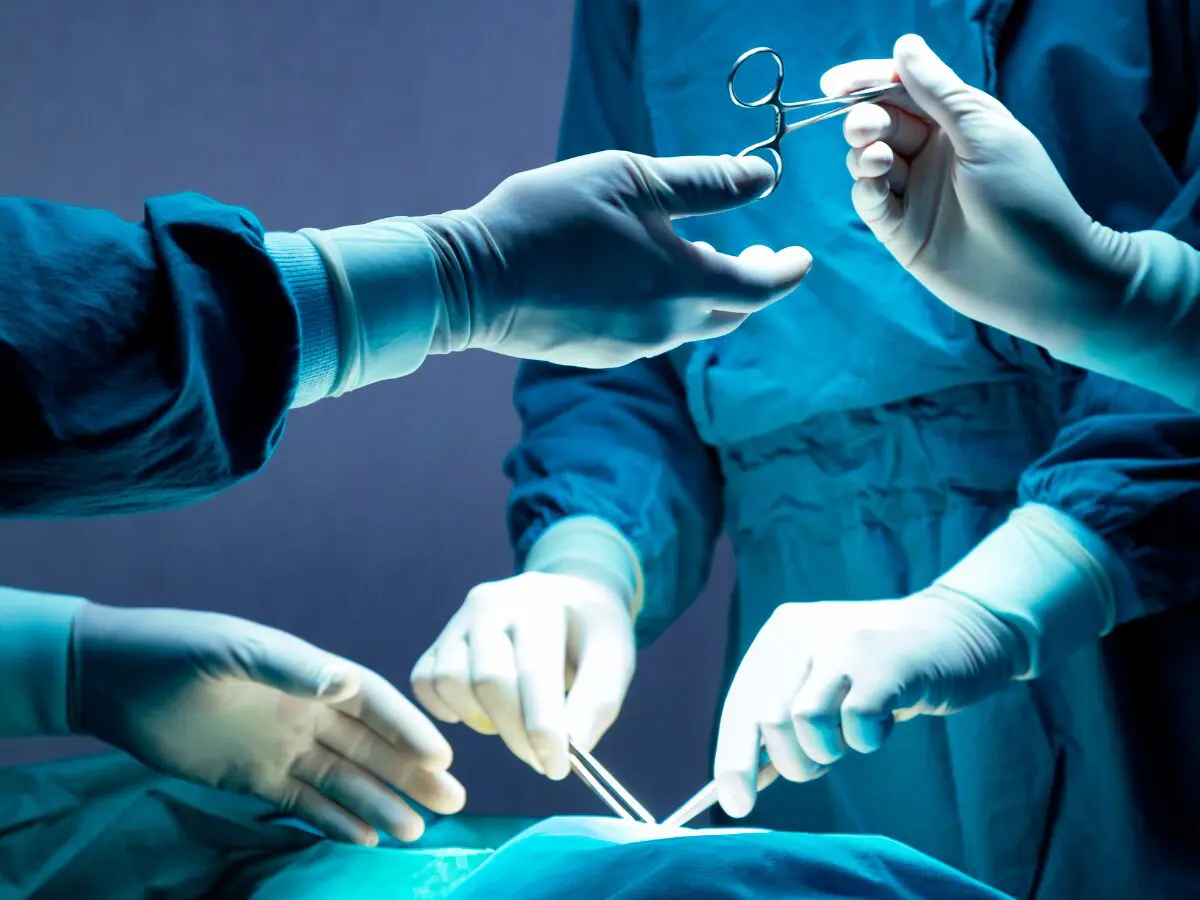 A close up of a surgery with surgeons passing themselves instruments with gloved hands.