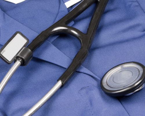 Close-up of a black stethoscope resting on blue medical scrubs with a blank name tag, symbolizing healthcare professionalism and patient care