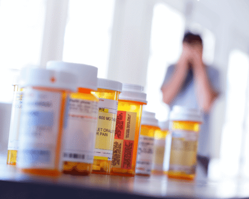 Prescription pill bottles on a table with a distressed person blurred in the background