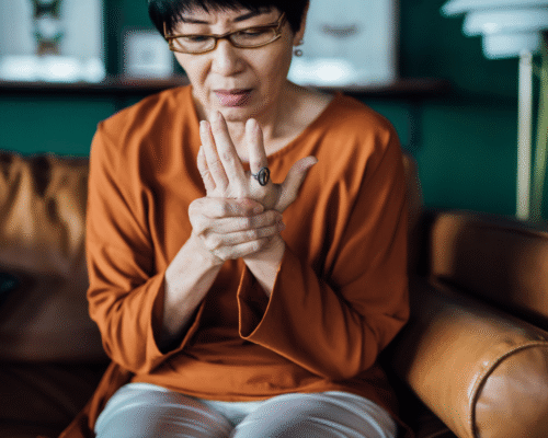 Older woman sitting on a couch, holding her wrist and looking at her hand in discomfort, representing a potential early symptom of stroke relevant to misdiagnosis awareness