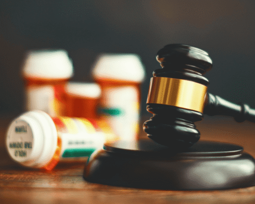 A black wooden gavel striking a wooden base, with four prescription pill bottles in the background