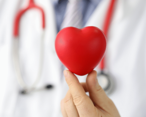A medical professional holding a red heart model in front of a stethoscope, representing cardiac care, diagnosis, and the importance of recognizing heart-related conditions in a clinical setting.