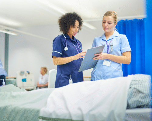 Two nurses reviewing a patient’s chart beside a hospital bed, illustrating potential nursing errors such as medication mistakes, delayed care, or inadequate monitoring.