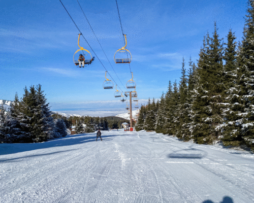 Ski lift carrying riders above a groomed ski slope surrounded by snow-covered trees, representing Colorado ski resorts, lift operations, and the potential safety hazards associated with ski lift accidents and operator negligence.