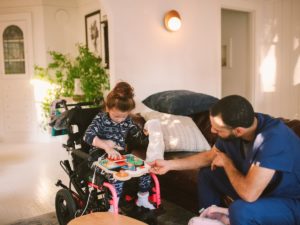 A girl with Cerebral Palsy sits playing wither her dad in a living room