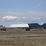 The architecturally distinctive white terminal teepees of Denver International Airport and the new glass hotel stand on the Colorado prairie with parking structures and roads leading to the airport.