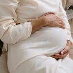 A pregnant woman holding her belly while sitting down.