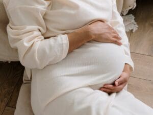 A pregnant woman holding her belly while sitting down.