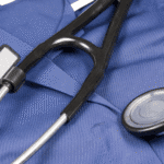 Close-up of a black stethoscope resting on blue medical scrubs with a blank name tag, symbolizing healthcare professionalism and patient care