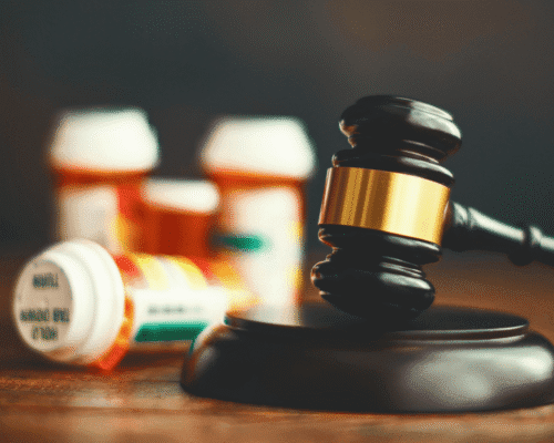 A black wooden gavel striking a wooden base, with four prescription pill bottles in the background
