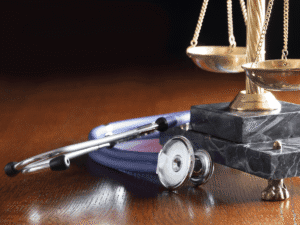Close-up of a stethoscope next to brass legal scales on a polished wooden surface, symbolizing the intersection of healthcare and legal accountability