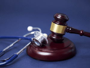 Close-up of a stethoscope next to brass legal scales on a polished wooden surface, symbolizing the intersection of healthcare and legal accountability