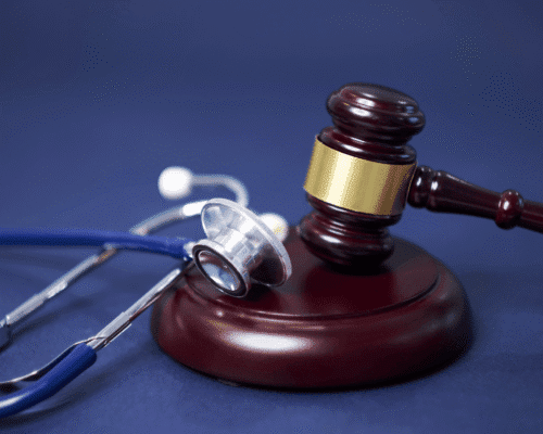 Close-up of a stethoscope next to brass legal scales on a polished wooden surface, symbolizing the intersection of healthcare and legal accountability