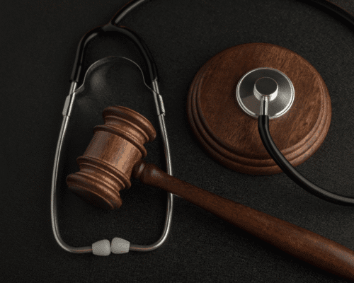 A wooden judge’s gavel rests beside a stethoscope on a dark surface. The composition symbolizes the intersection of law and medicine, representing medical malpractice cases and the pursuit of justice for patients harmed by negligence.