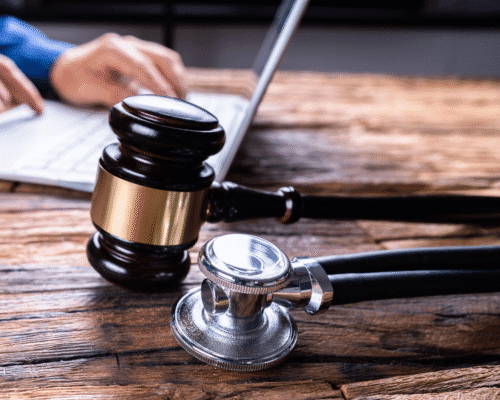 wooden gavel and stethoscope rest on a wooden desk near a person typing on a laptop. The image symbolizes the intersection of medicine and law, representing medical malpractice cases involving misdiagnosis and delayed diagnosis.
