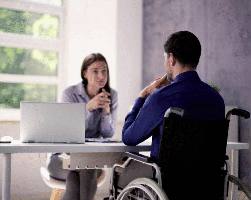 A woman sits across a desk from a man in a wheelchair, engaged in a serious conversation in a bright office setting. The image represents legal consultations in Denver for catastrophic car crash victims, focusing on proving pain, suffering, and non-economic damages through documentation and expert evidence.