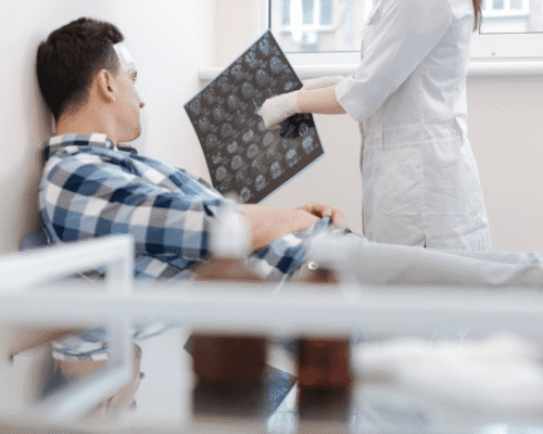 Patient with a head injury in a hospital bed reviews brain scan images with a medical professional, illustrating long-term traumatic brain injury effects in Colorado.