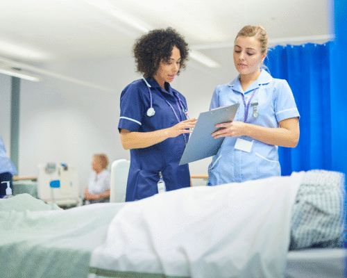 Two nurses reviewing a patient’s chart beside a hospital bed, illustrating potential nursing errors such as medication mistakes, delayed care, or inadequate monitoring.