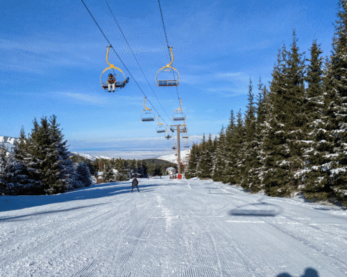 Ski lift carrying riders above a groomed ski slope surrounded by snow-covered trees, representing Colorado ski resorts, lift operations, and the potential safety hazards associated with ski lift accidents and operator negligence.